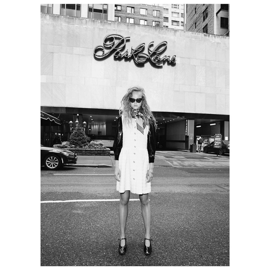 Woman in white dress and sunglasses stands on city street in front of 'Park Lane' sign, captured in black and white, urban fashion shot.