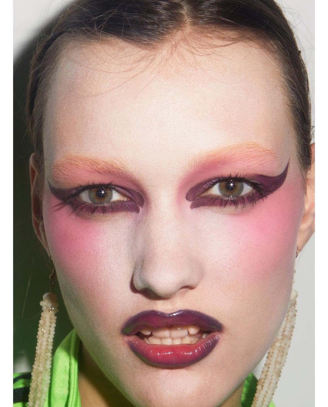 Close-up portrait of a woman with dramatic pink and purple eye makeup, bleached eyebrows, and glossy lips by Carin Backoff.