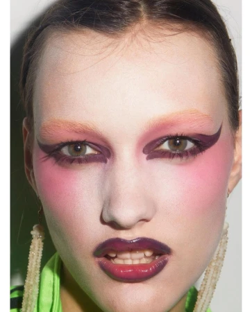 Close-up portrait of a woman with dramatic pink and purple eye makeup, bleached eyebrows, and glossy lips by Carin Backoff.