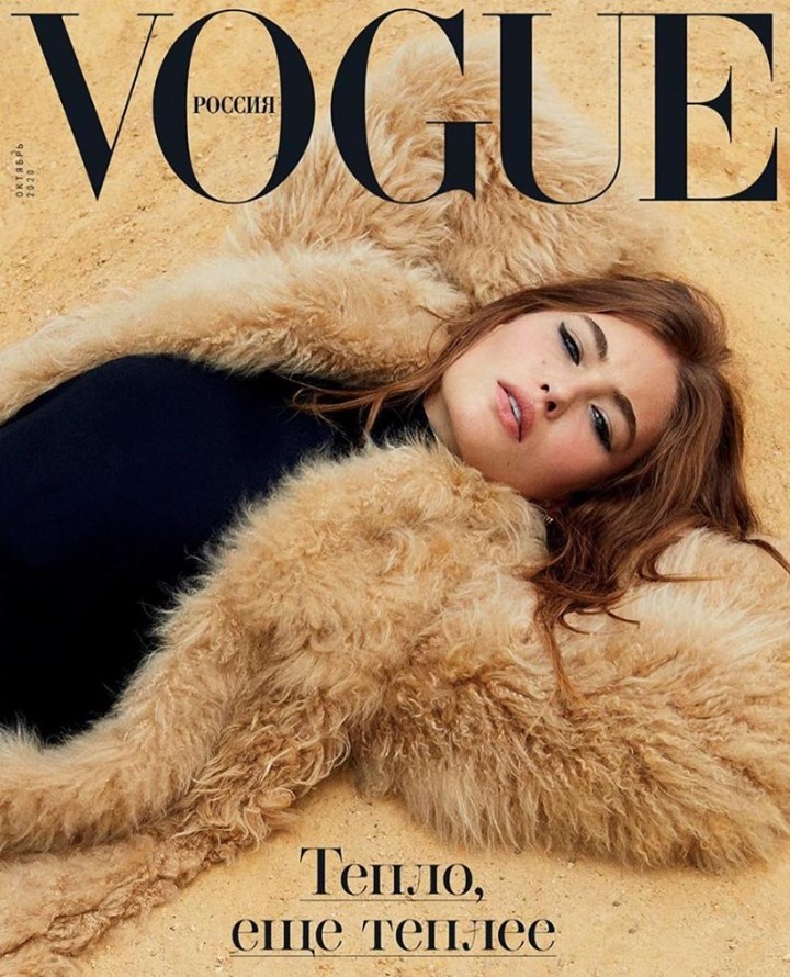 Model lying down on a sandy ground wearing a fluffy tan fur coat and black top, photographed by Carin Backoff.