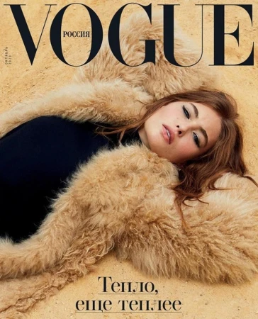 Model lying down on a sandy ground wearing a fluffy tan fur coat and black top, photographed by Carin Backoff.