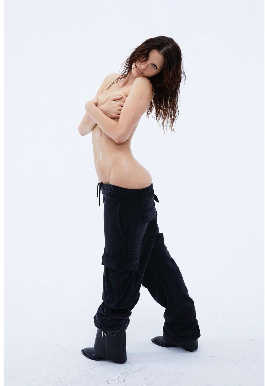 Portrait of woman posing with black pants and boots against a plain white backdrop, looking into the camera with arms crossed.