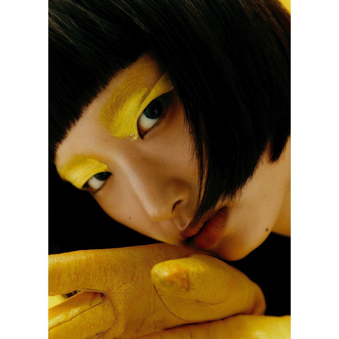 Close-up portrait of a young Asian woman with dark hair and vivid yellow eye makeup, showcasing a bold and artistic beauty look.