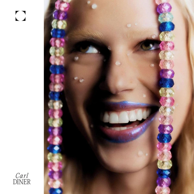 Close-up of a woman with fair skin and blue lipstick smiling with beaded strings, small white decorative dots and a white background.