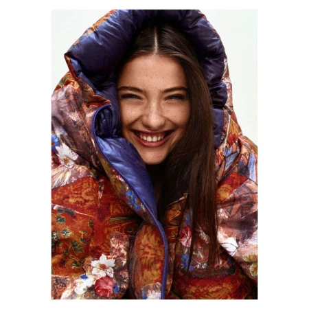 Smiling woman wearing a floral puffer jacket with a hood. Head and shoulders shot, indoors. Beauty and fashion portrait.