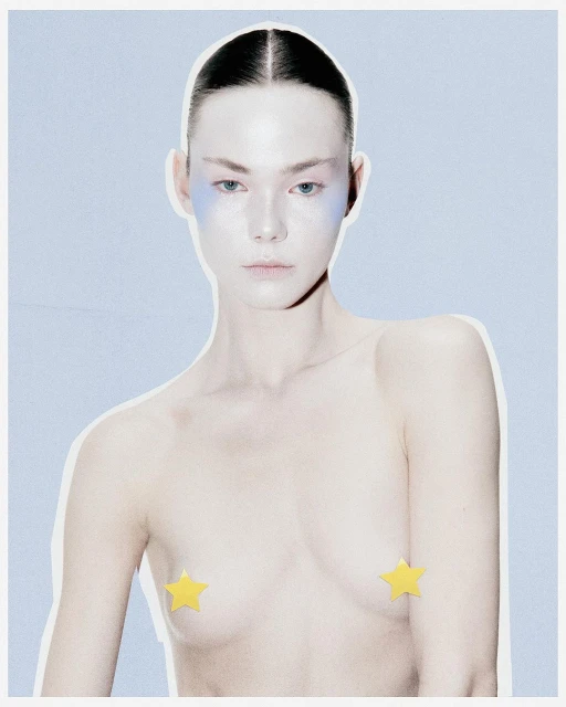 Conceptual beauty shot of a topless adult woman with blue face makeup and yellow star nipple pasties against a light blue background.