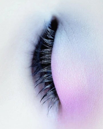 Macro shot of a closed eye with long, dark eyelashes and light skin with soft pink eyeshadow, showcasing beauty and makeup artistry.