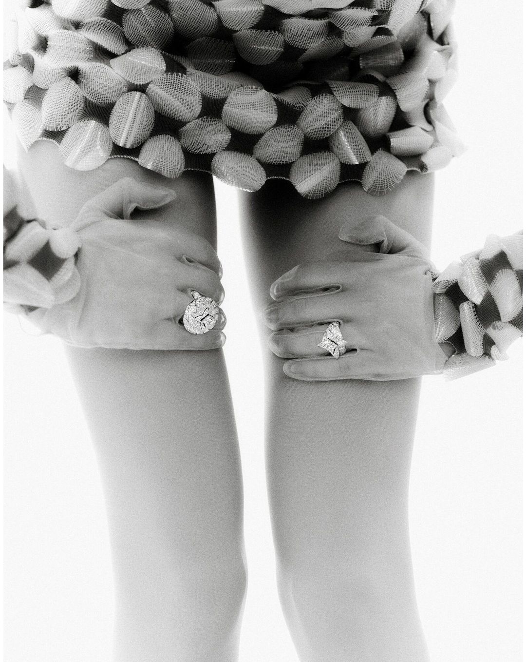 Close-up of an abstract, black-and-white fashion photograph featuring human legs and gloved hands adorned with large, sparkly rings.