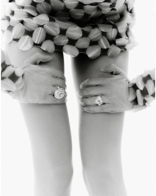 Close-up of an abstract, black-and-white fashion photograph featuring human legs and gloved hands adorned with large, sparkly rings.