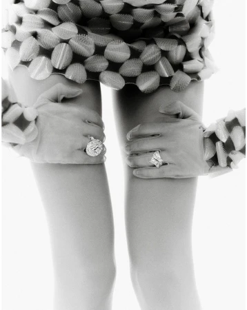 Close-up of an abstract, black-and-white fashion photograph featuring human legs and gloved hands adorned with large, sparkly rings.