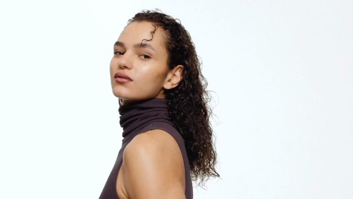 Portrait of a woman with dark curly hair and a dark turtleneck top against a plain white background by Carl Diner