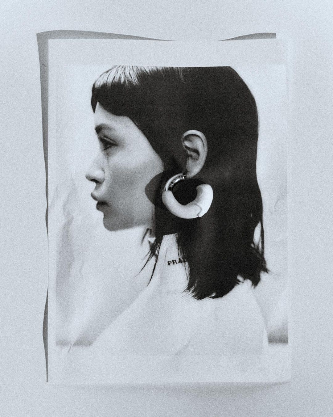 Monochrome portrait of a woman in profile wearing large hoop earrings, with short dark hair, against a neutral textured backdrop.