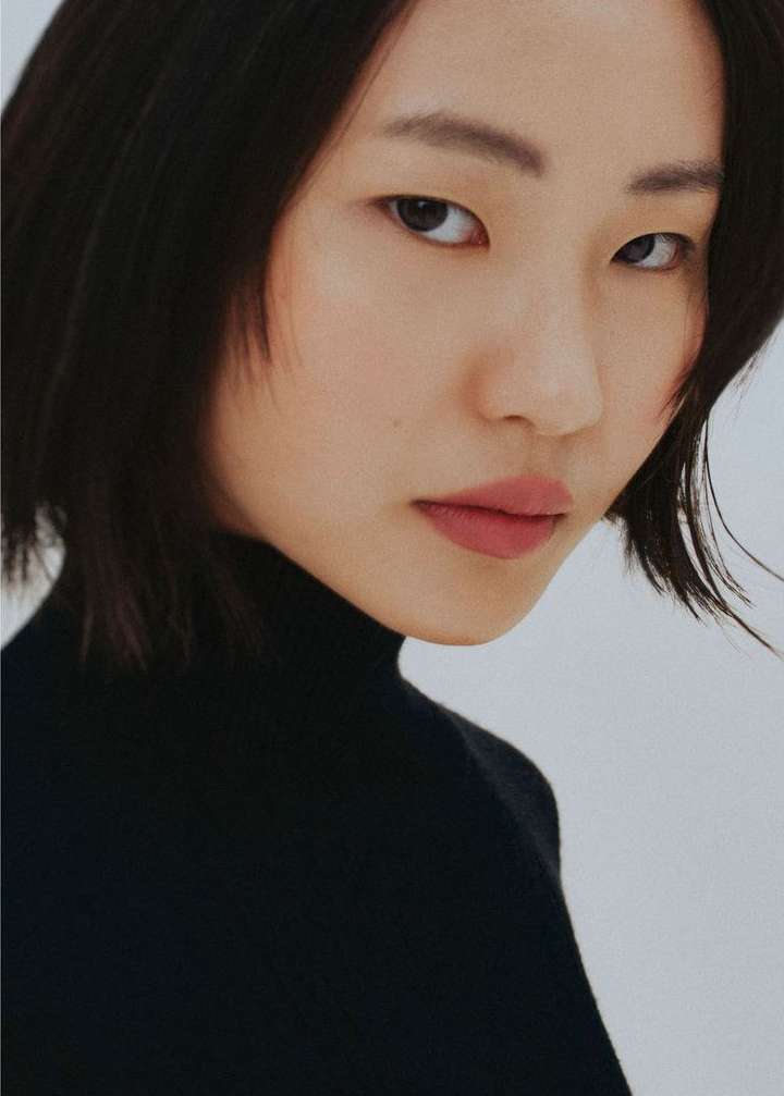 Portrait of an Asian woman with short dark hair wearing a black turtleneck against a neutral background.