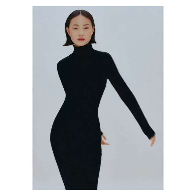 A slender Asian woman posing in a sleek black turtleneck dress against a bright white backdrop in a minimalist studio fashion shot.