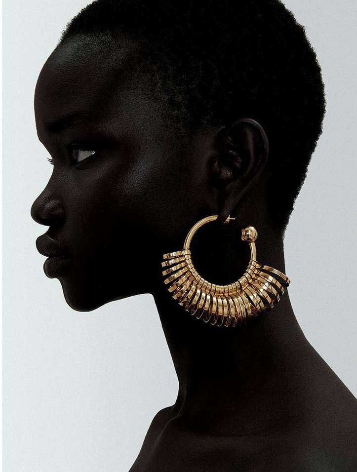 Profile of an African woman wearing large golden hoop earrings against a neutral background in a beauty or fashion context.