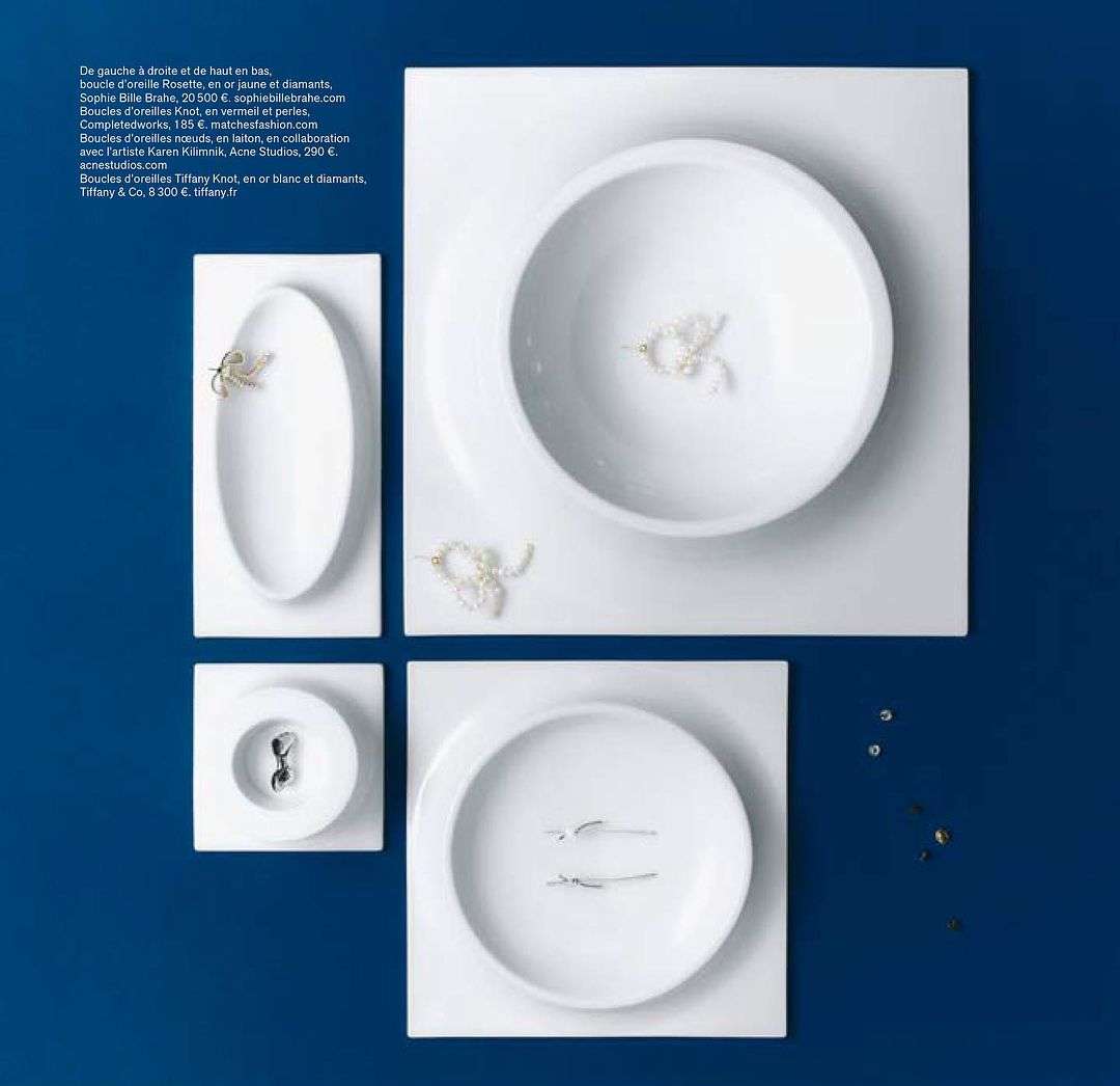 Overhead shot of white ceramic plates and bowls on a dark blue background, each containing fine jewellery.