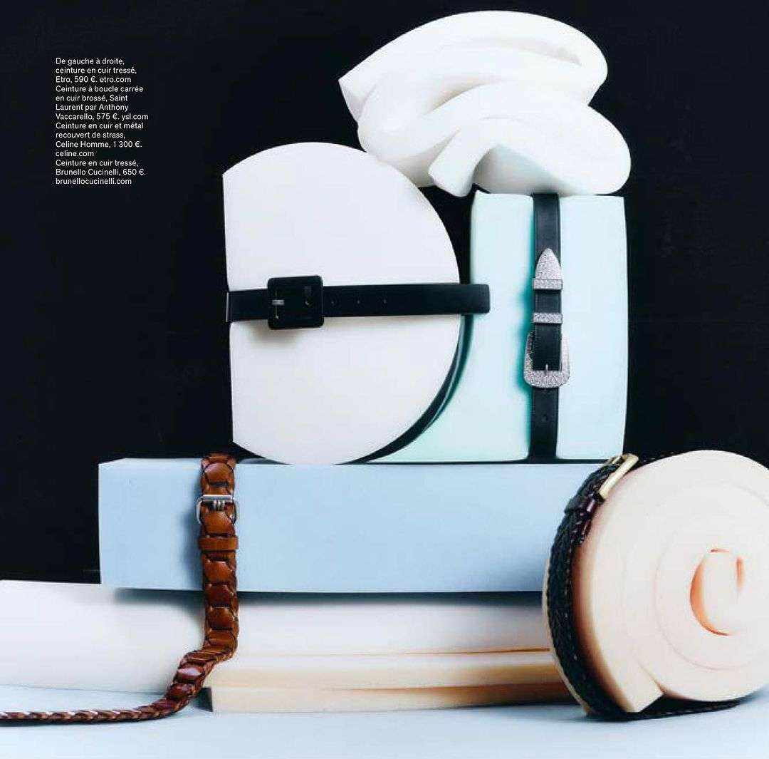 Still life of assorted belts with buckles, artfully arranged on stacked white and light blue blocks against a black backdrop.