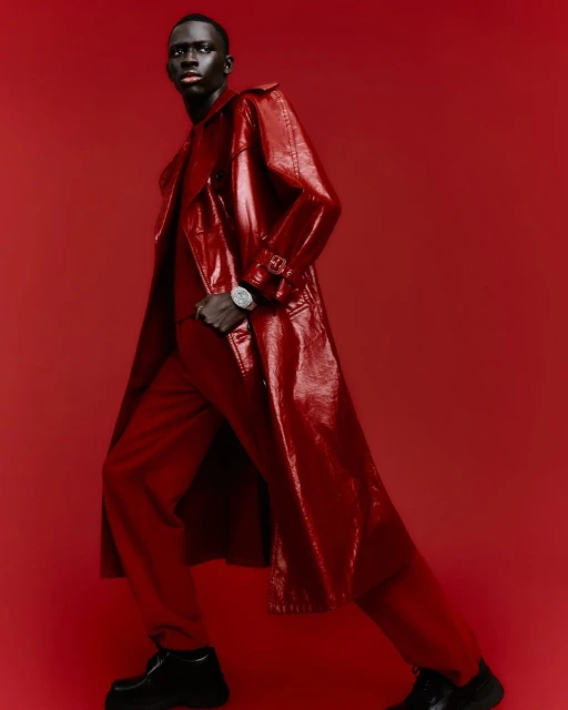 Fashionable man in a glossy red trench coat and trousers against a matching backdrop, showcasing modern style and texture.