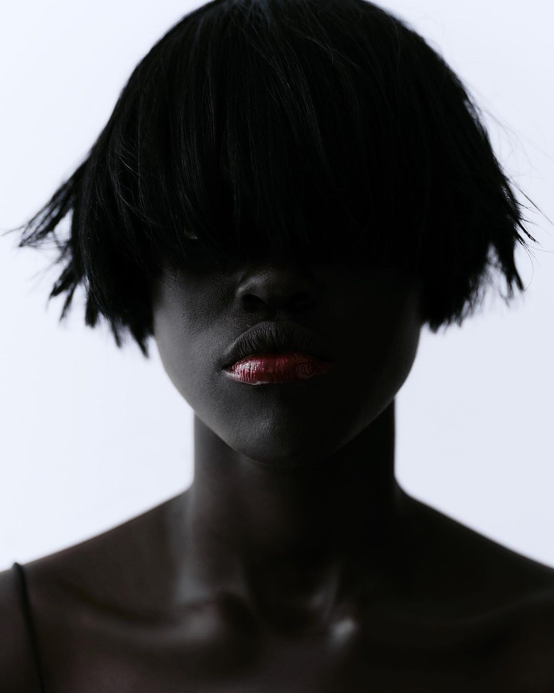 Portrait of woman with dark skin and short dark hair against a plain background, showcasing makeup and dark hair. Beauty aesthetic.