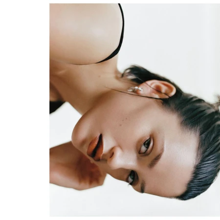 Close-up portrait of a woman with dark hair and dark lipstick photographed vertically against a bright white background