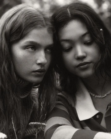 Close-up black and white portrait of two young women with dark hair posing closely together outdoors.
