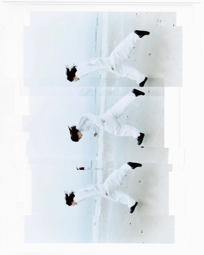 A multi-exposure photographic collage of a model jumping against a light beach background, wearing a white jumpsuit and black shoes.