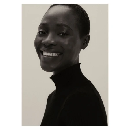 Portrait of a smiling Black woman with short hair wearing a black turtleneck against a neutral background by Carl Diner