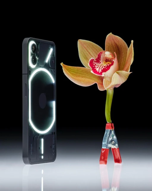 Nothing Phone (2) with illuminated glyph interface next to an orchid held by metal clips against a dark reflective backdrop.