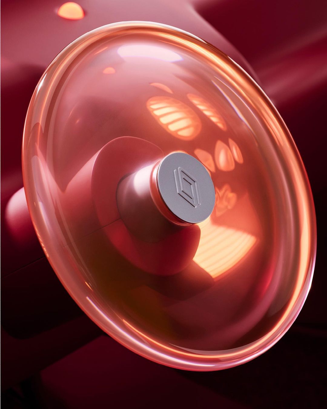 Close-up of a translucent red domed object with a silver cylindrical base and a square logo in a studio setting with soft lighting.