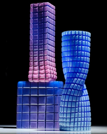 Three stacked and standing glass sculptures with grid patterns in shades of blue and purple against a dark background