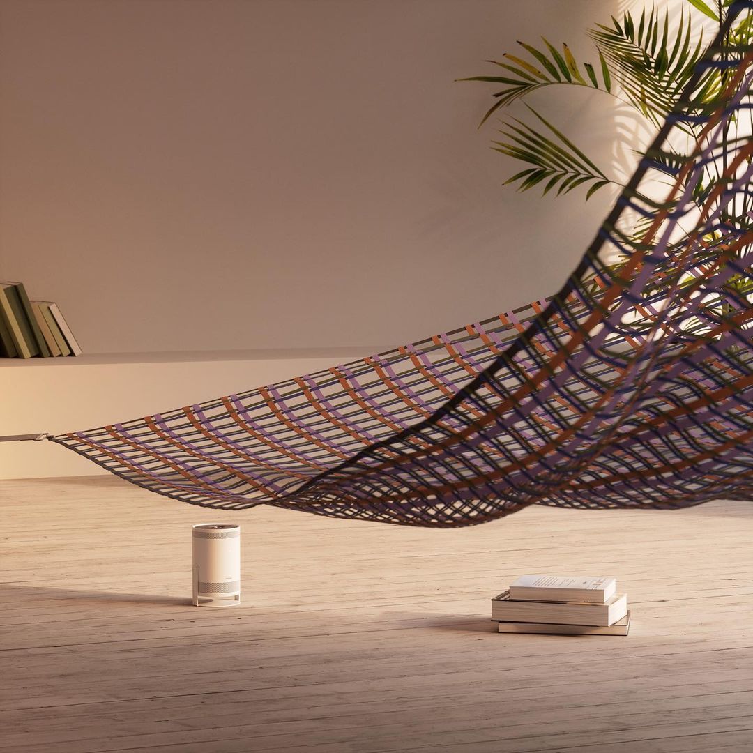 Modern home interior with a decorative hammock, books, air purifier and potted plant on wooden floor against a white wall.