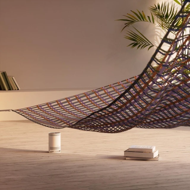 Modern home interior with a decorative hammock, books, air purifier and potted plant on wooden floor against a white wall.