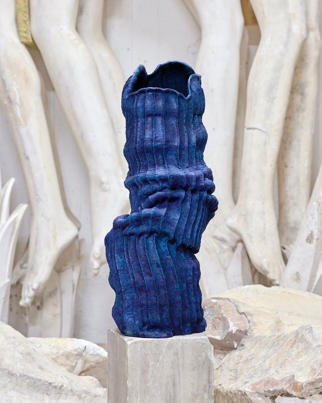Striking blue textured vase on a pedestal against a sculpted wall in a studio setting. Modern art with classical elements.