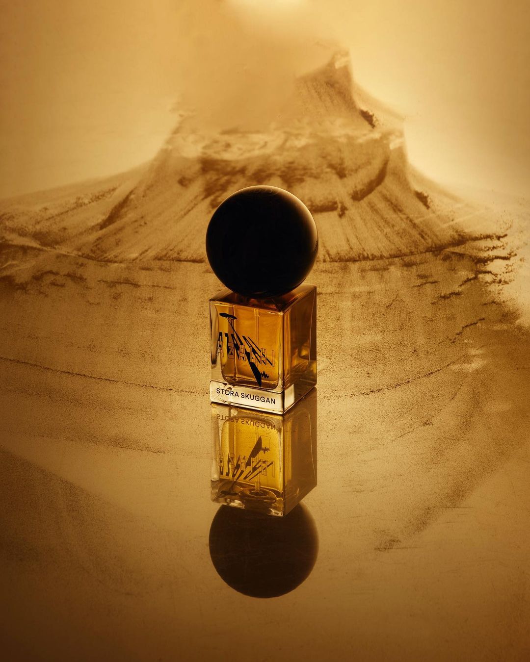 Perfume bottle on a reflective surface with a mountain in the background, against a beige and gold color palette. Product photography.