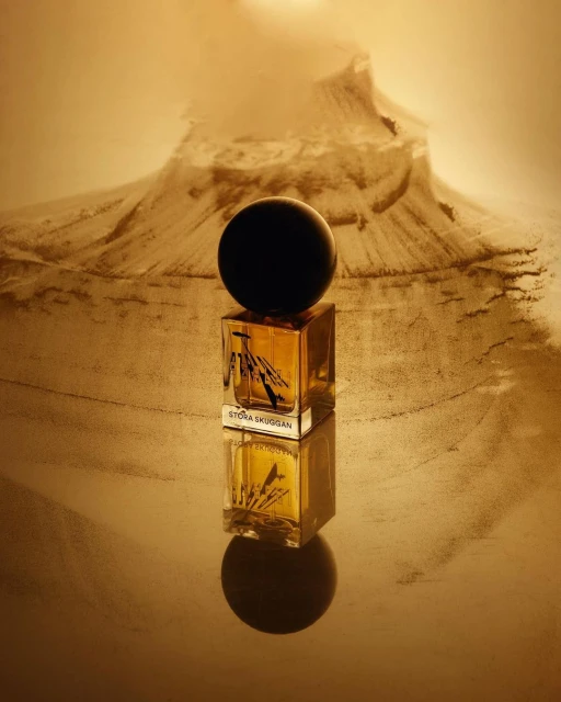 Perfume bottle on a reflective surface with a mountain in the background, against a beige and gold color palette. Product photography.