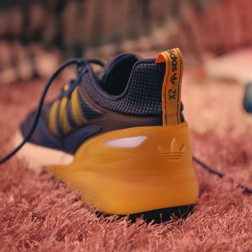 An Adidas running shoe in blue and yellow rests on a shag carpet.  Adidas brand logo is seen on the shoe's heel.