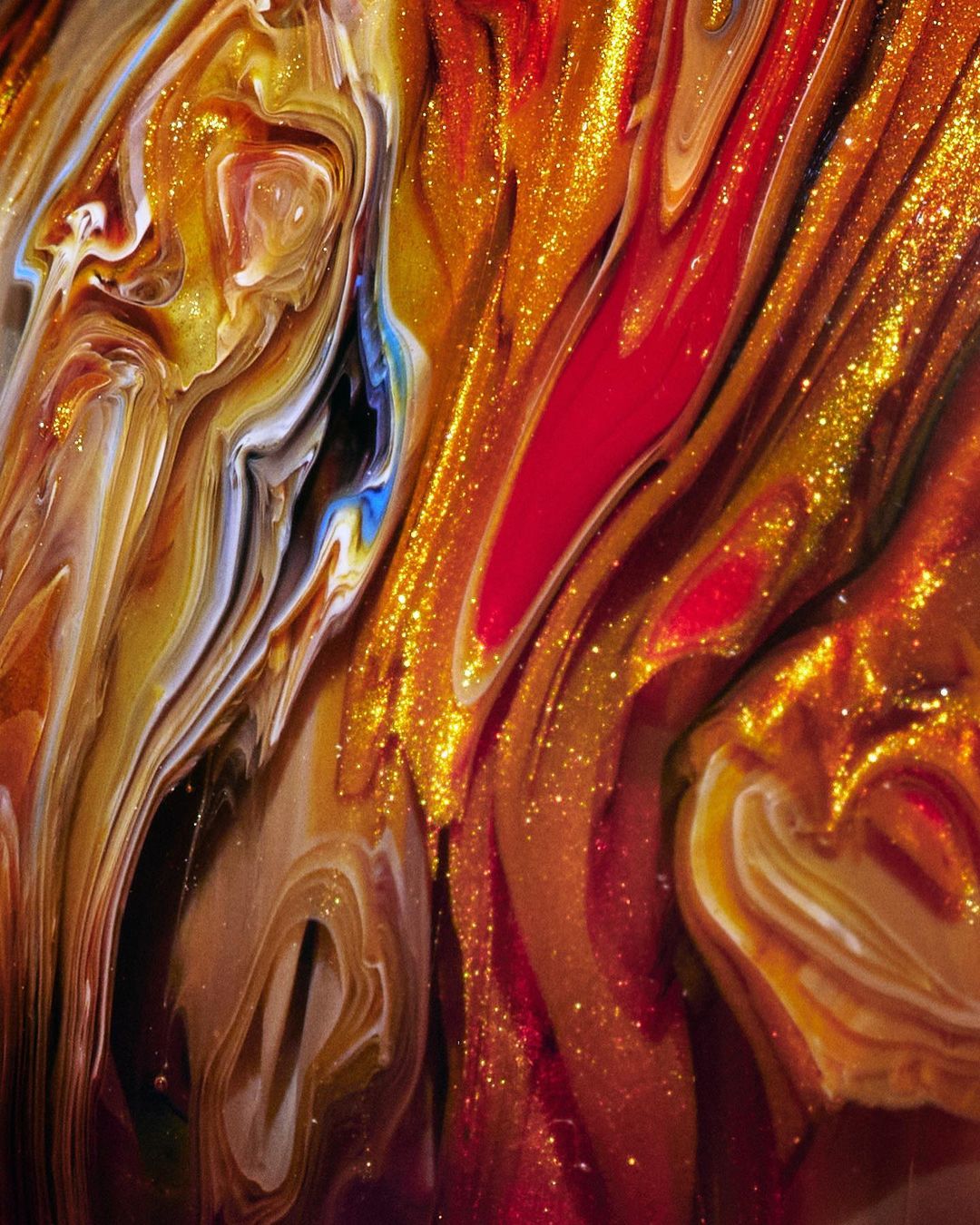Abstract liquid art featuring swirling patterns of gold, red, bronze, and white paint creating a textured, dynamic composition.