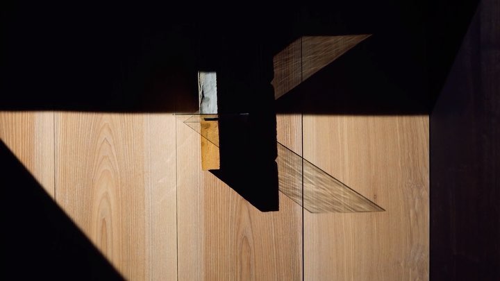 Abstract architectural shot featuring wood panelling, light and shadow, and a glass ledge with a small object.