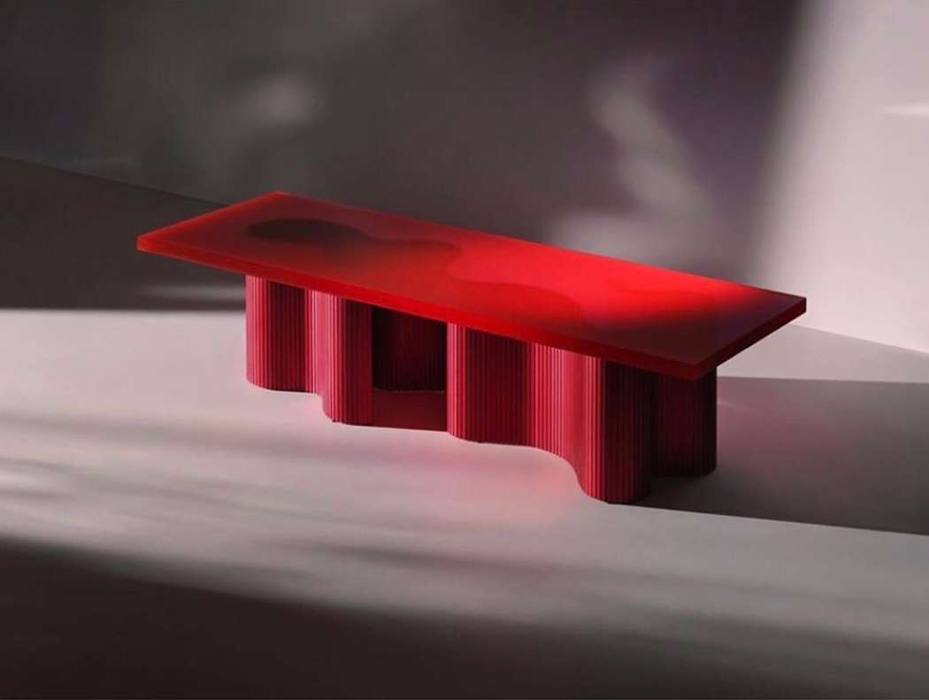 Modern red acrylic console table with reeded cylindrical legs, illuminated by natural light and shadows in a minimalist interior space.