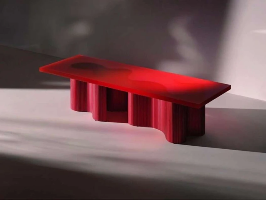 Modern red acrylic console table with reeded cylindrical legs, illuminated by natural light and shadows in a minimalist interior space.