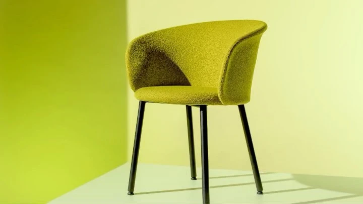 Lime green upholstered armchair with black metal legs set against a pale yellow background