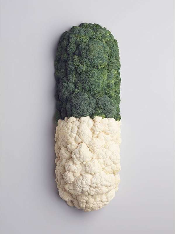 Overhead studio shot of capsule-shaped composition of broccoli and cauliflower florets on gray backdrop for food or health concept.