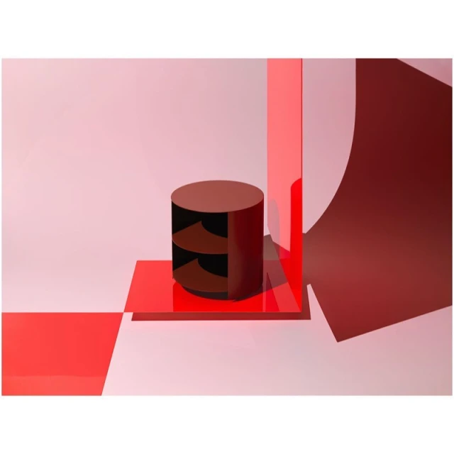 Abstract product shot with a round burgundy display table and geometric shapes against a light pink background in a photo studio setting.