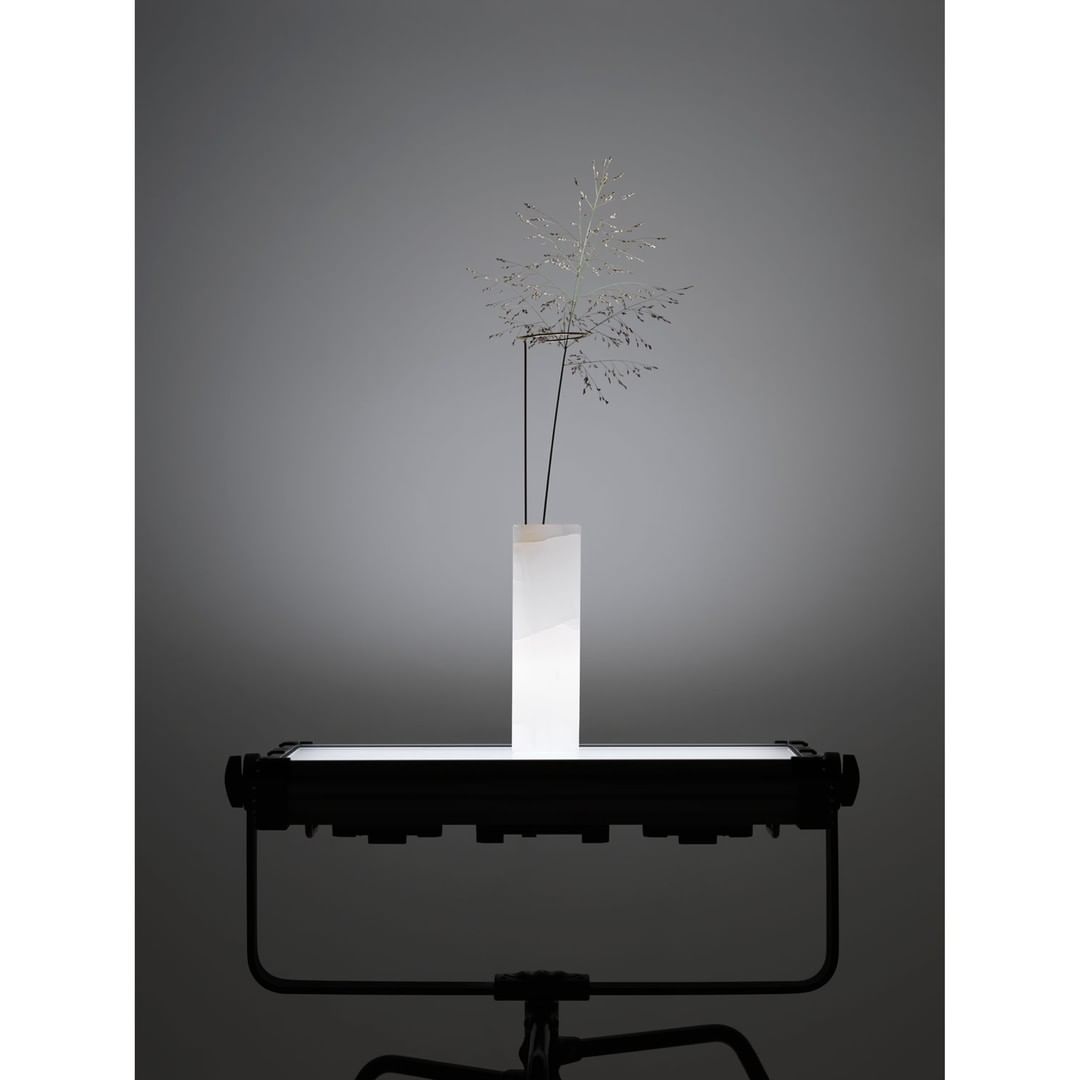 Stylized photography featuring a white vase with delicate silver floral elements, set on a black platform against a neutral backdrop.