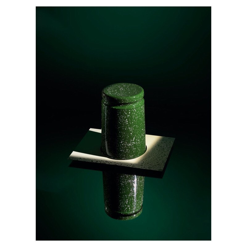 Green and white speckled enamel container with lid on a white platform reflecting on a glossy green surface, lit with dramatic lighting.