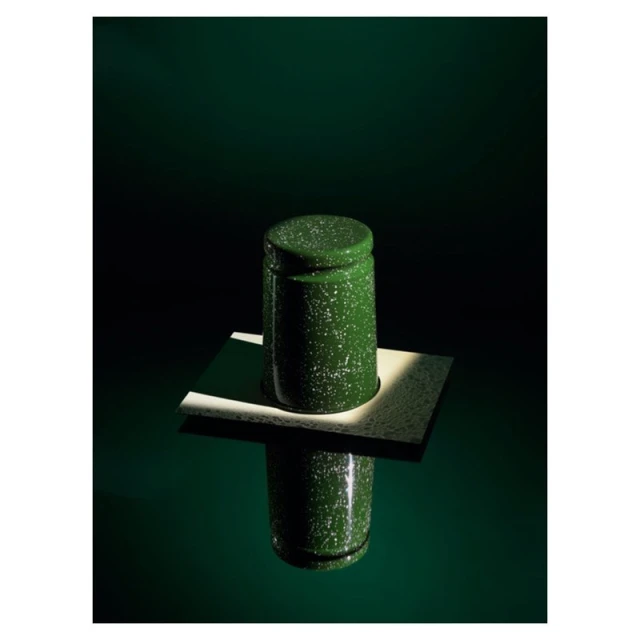 Green and white speckled enamel container with lid on a white platform reflecting on a glossy green surface, lit with dramatic lighting.