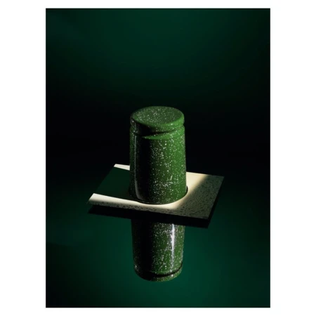 Green and white speckled enamel container with lid on a white platform reflecting on a glossy green surface, lit with dramatic lighting.