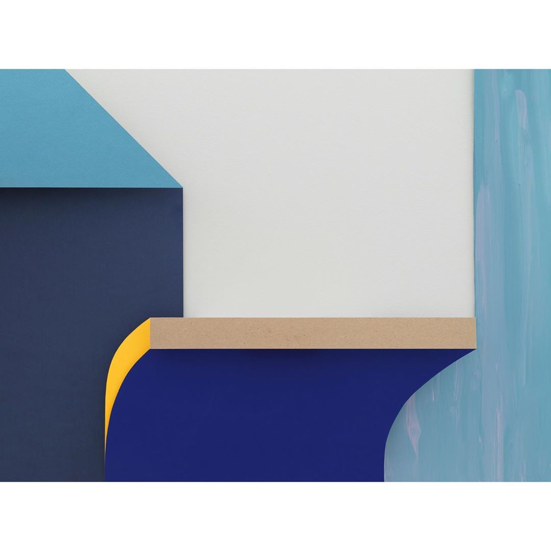 Abstract geometric wall art featuring a layered composition of dark blue, light blue, yellow, brown, and white shapes on a blue background.
