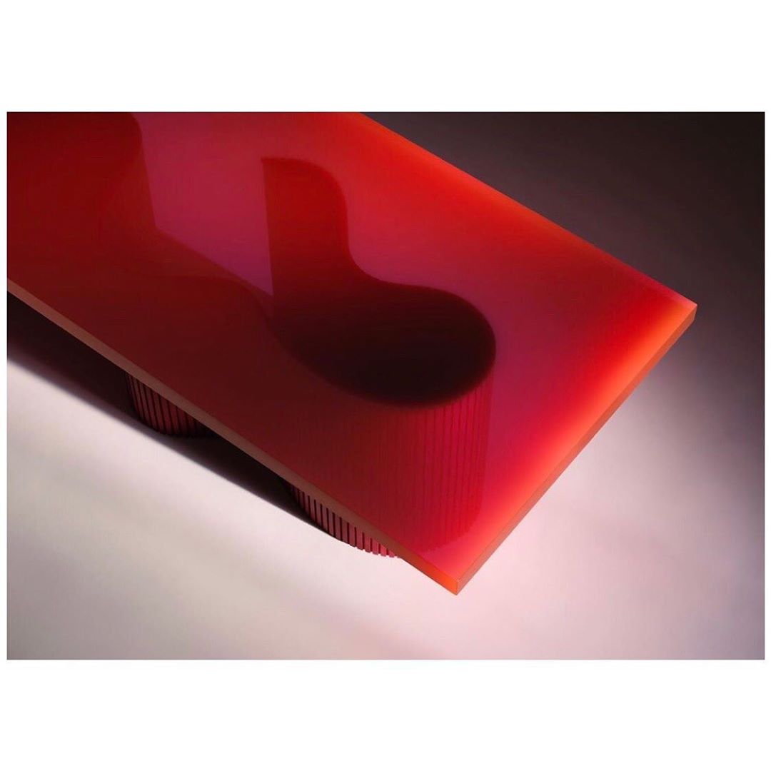 Abstract close-up of a red rectangular table with rounded corners, supported by multiple cylindrical legs, set against a gray gradient background.