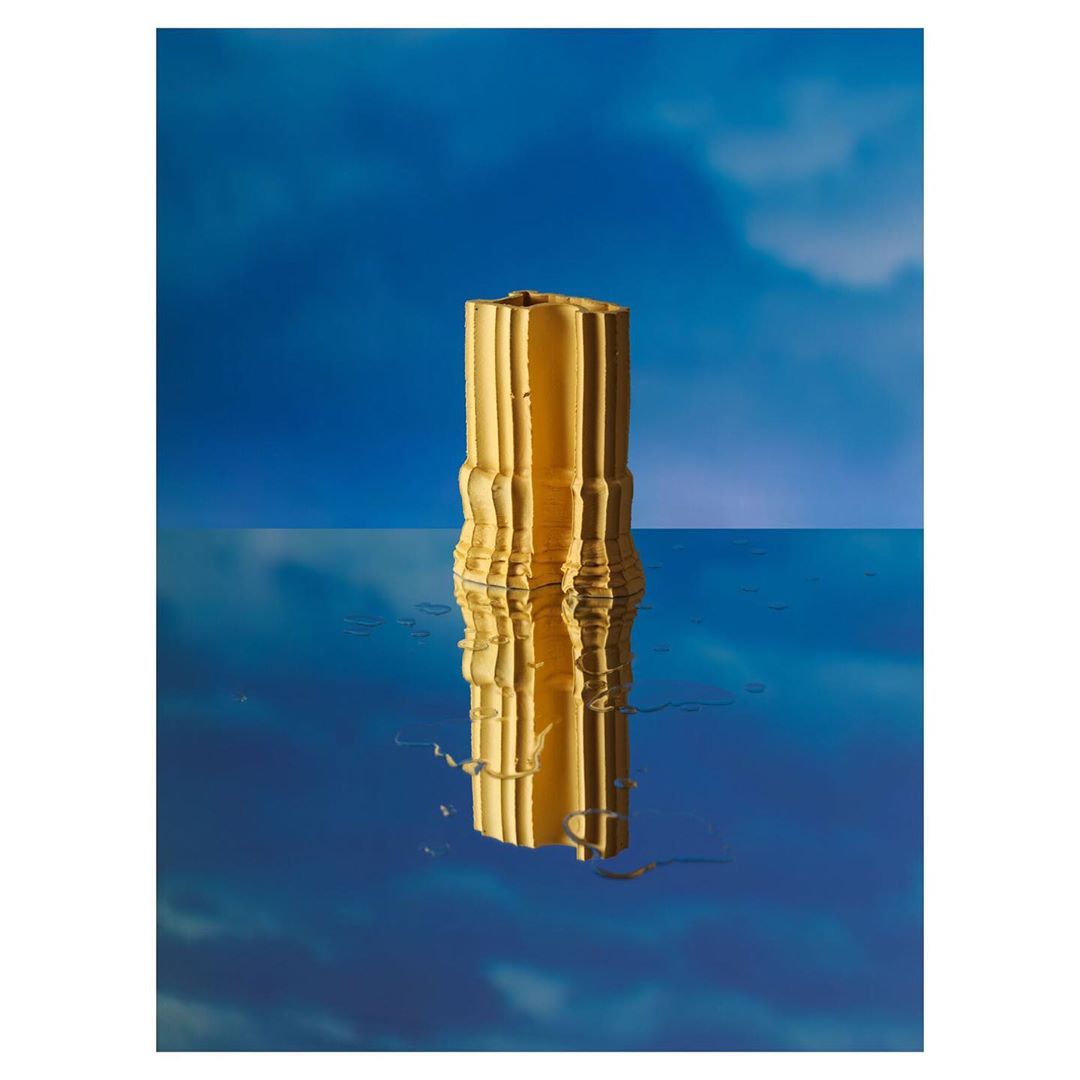 Abstract product shot of a reflective gold vase sitting on a reflective surface, with a blurred blue background and atmospheric lighting.